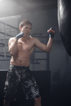 Young man doing boxing workout in the gym. Male fighter smash punching bag.
