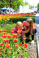 sister teaches the younger to smell tulips on the city flowerbed