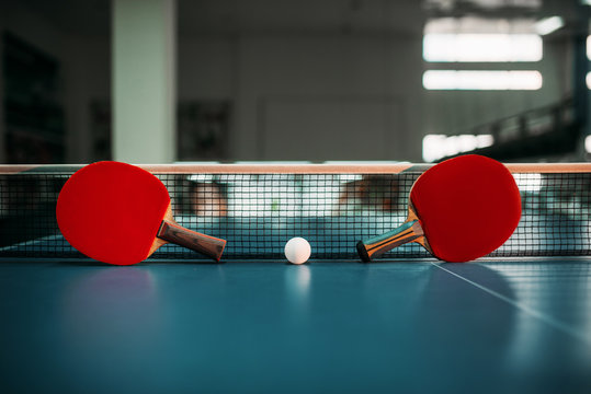 Two tennis rackets and ball against net on table