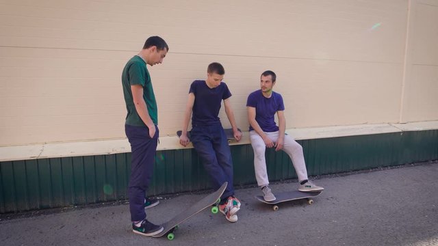 Young men rest near the house after a long trip on skateboards, adult guys sit on the steps of the house after performing complex tricks on the board