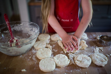 Girl pressing cookie cutter into dough on tabletop 