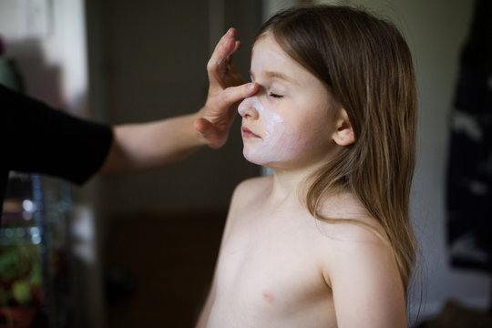 Mother applying cream to daughters face