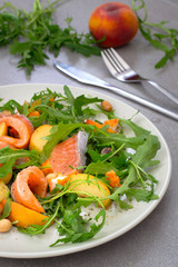 Salad with salmon, arugula, peach and peanuts. Rustic style. Gray stone background. Close-up. Top view