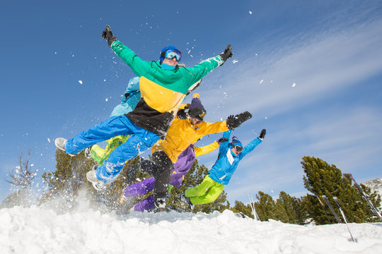 Group of happy friends having fun jumping to snow. Ski and snowboard holiday