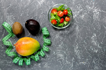 Healthy diet. Salad and fruits mango, mangosteen and measuring tape on stone table top view copyspace