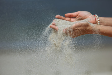 Female hands releasing dropping sand. Sand flowing through the hands against blue ocean. Summer beach holiday vacation concept