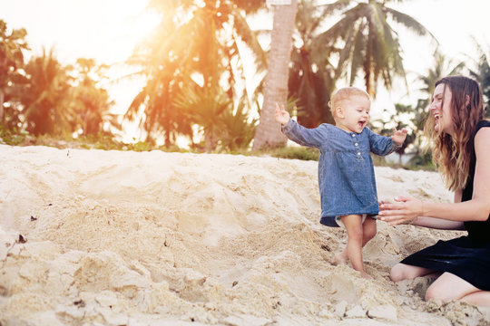 Happy Mother playing with baby Girl on tropical beach under palm trees. Travel with kid, summer holiday