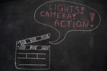 Open movie clapper and speech bubble with lights, camera, action writing drawn with chalk on blackboard