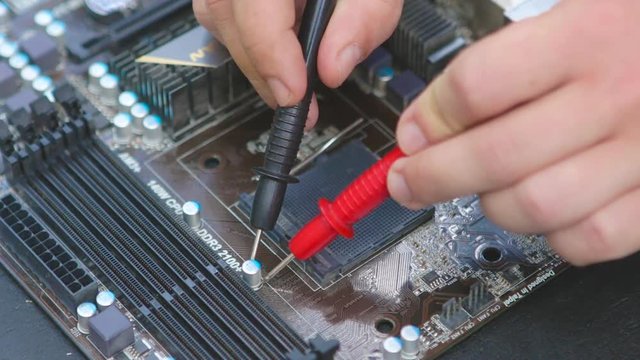 Service man cheking \ diagnosing motherboard chips with multimeter.