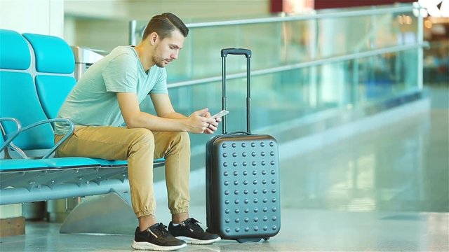 Young man in an airport lounge waiting for flight aircraft. Caucasian man with smartphone in the waiting room