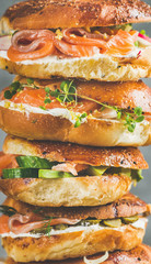Heap of Bagels with salmon, eggs, vegetables, capers, fresh herbs and cream-cheese, grey concrete background, vertical composition. Healthy breakfast, lunch or take-away food concept