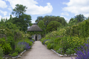 The 19th Century thatched round house surrounded by beautiful flower beds and gravel paths in the walled garden at West Dean gardens in Hampshire, England 