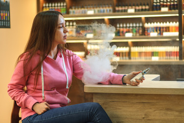 Vape woman. Portrait of young cute girl in pink hoodie smoking an electronic cigarette in the bar.