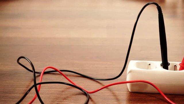 Measurement of voltage in electrical socket extension cord with multimeter on wooden floor background 4K ProRes HQ codec