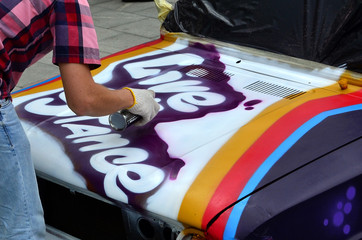 A young red-haired graffiti artist paints a new colorful graffiti on the car. Photo of the process...