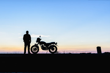 Silhouette of man and a motorcycle with sunset background
