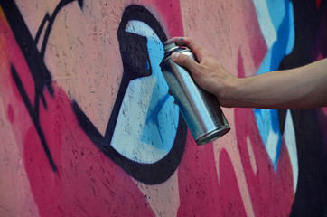 A hand with a spray can that draws a new graffiti on the wall. Photo of the process of drawing a...