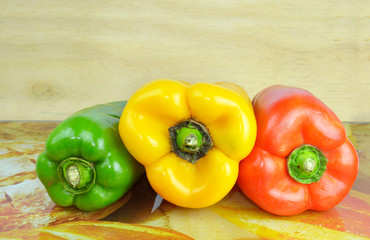 Pile of three different kinds of bell peppers against a wood background