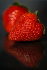 Red strawberries on black glossy background with reflection