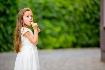 A little girl in a white dress is eating ice cream.