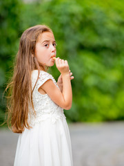 Fototapeta premium A little girl in a white dress is eating ice cream.