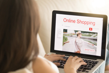 Woman lying on sofa with laptop pc visits apparel store web page in Internet. Female customer shopping trendy clothes. Girl buying elegant wear on seasonal sale online. Close up view over the shoulder