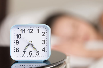 Close up image of modern alarm clock on bedside table with blurred person sleeping in bed in background. Wake up in early morning, stable sleep routine, healthy sleep schedule, wake-up time concept