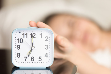 Close up picture of square alarm clock on bedside table showing seven o'clock AM with blurred...