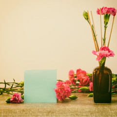 Bright pink carnations flower in the japanese glass vase on table and blank blue card . Vintge image style
