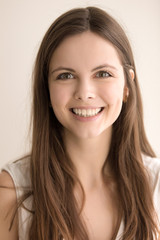 Fototapeta premium Headshot portrait of happy young woman. Charming teen girl with joyful facial expression looking at camera with beautiful smile. Pretty lady feeling enthusiasm and admiration. Close up. Front view