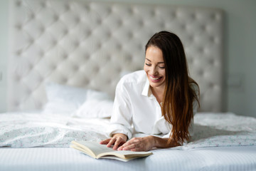 Young woman at home on bed reading book