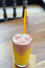 A glass of fresh fruit smoothie with milk, made from mango and strawberry topped with mint leaves on wooden table.