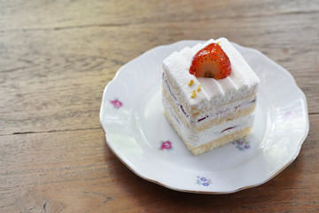 Homemade strawberry cake and cream topped with fresh strawberry on wooden table background.