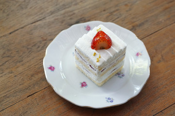 Homemade strawberry cake and cream topped with fresh strawberry on wooden table background.