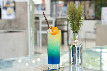 A glass of Iced mixed blue hawaii soda with lemonade, orange juice and honey on table and on blurred background, Colorful Cocktail or Tropical Mocktail.