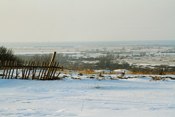 Old rickety fence against the background of a winter field in the horizon