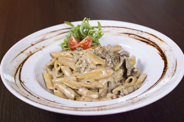 Pasta with tomatoes, meat and parmesan on a plate close-up on the table. Penne pasta in tomato sauce with chicken, tomatoes decorated with parsley on a wooden table.