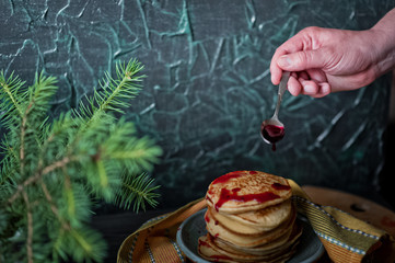 Beautiful homemade pancakes with strawberries and raspberry red jam on a black wall background. Pancakes with fresh juicy strawberries and a vase with a sprig of Christmas trees. Pancakes watered with