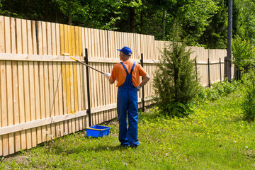 Male painter works at wooden fence in the garden