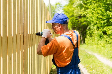 Close up portrait of skilled worker building wooden fence with cordless electric screwdriver