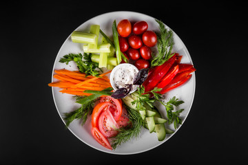 Assortment of fresh vegetables on a plate. On a dark background, top view.