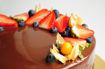 Cake in chocolate with strawberries, blueberries and physalis. Close-up. Picture for a menu or a confectionery catalog.