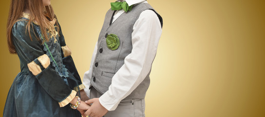 Little boy and girl in english traditional uniform holding each other hands on yellow background