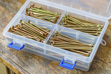 Long self-tapping screws in transparent plastic storage box on a wooden bench