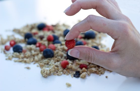 fingers holding wild strawberries and muesly