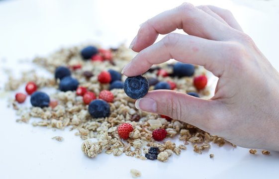 fingers holding bluberries and muesly