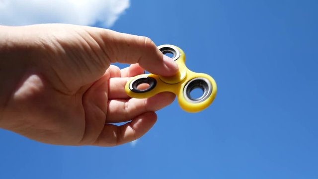 Fidget Spinner on a Sunny Day on the Background of the Blu Sky With Clouds. Toy for Increased Stress Relief. Hand Finger Spinner