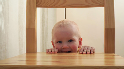 Cute little boy peeking out from behind a chair