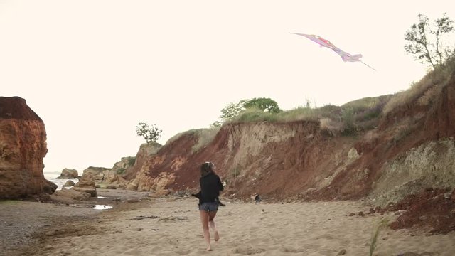 Young hipster woman releasing colorful kite on the beach in the evening. Slowmotion shot