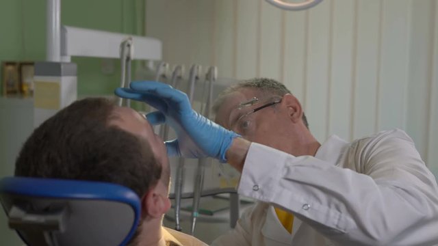 Dentist in a Face Mask Works a Drill in the Mouth of the Patient Sitting in the Dental Chair
